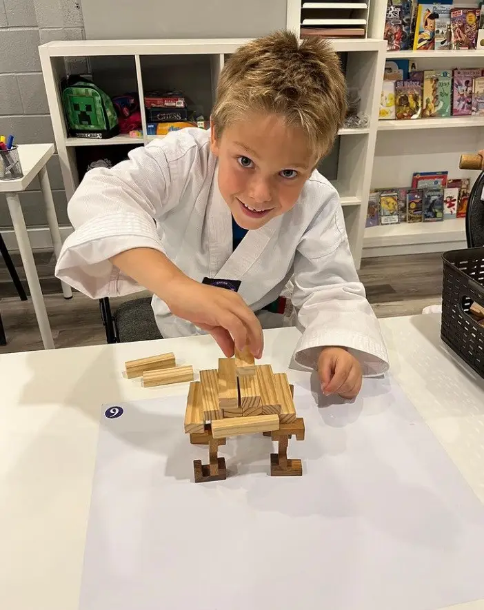A student in uniform building a tower of wooden blocks at a table