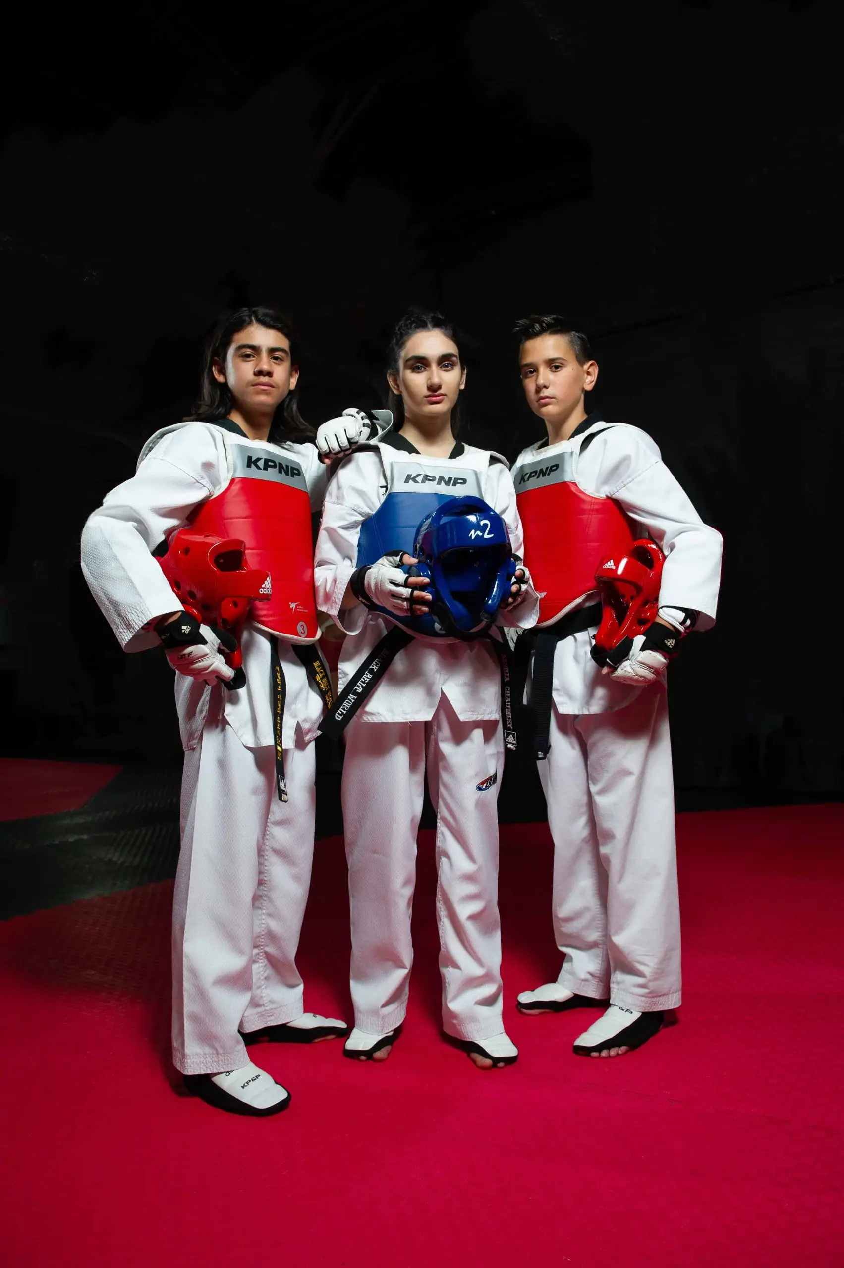 Three Dragon Taekwondo athletes in electronic chest protectors, holding their helmets