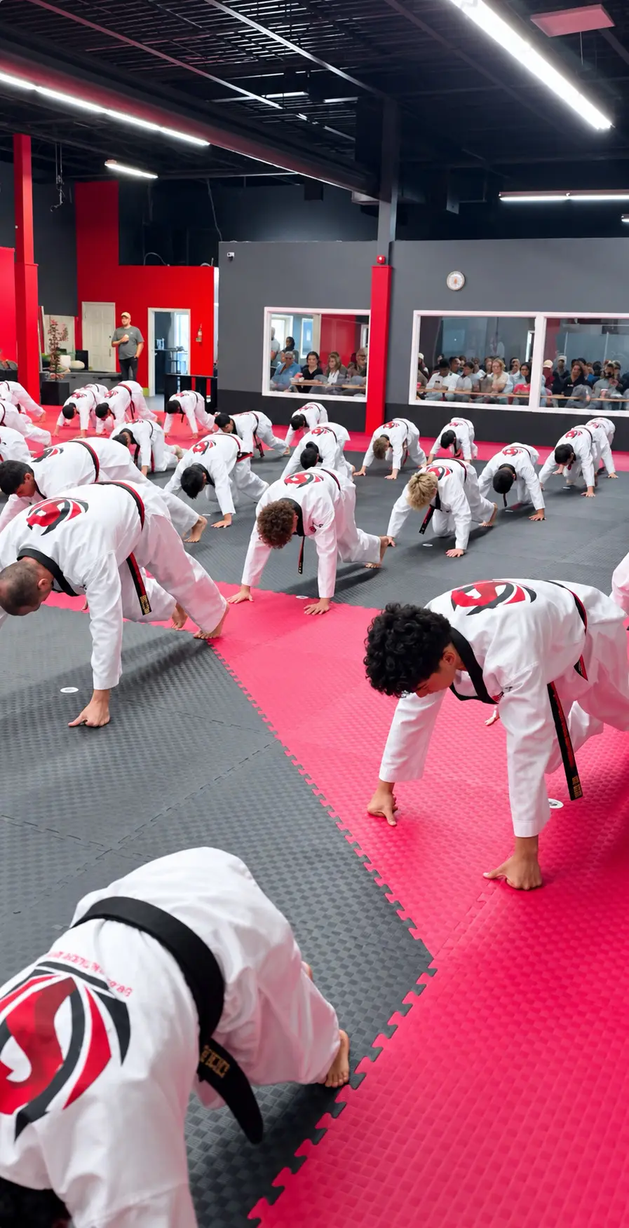 A class doing push-ups on the mats while parents watch through the viewing windows