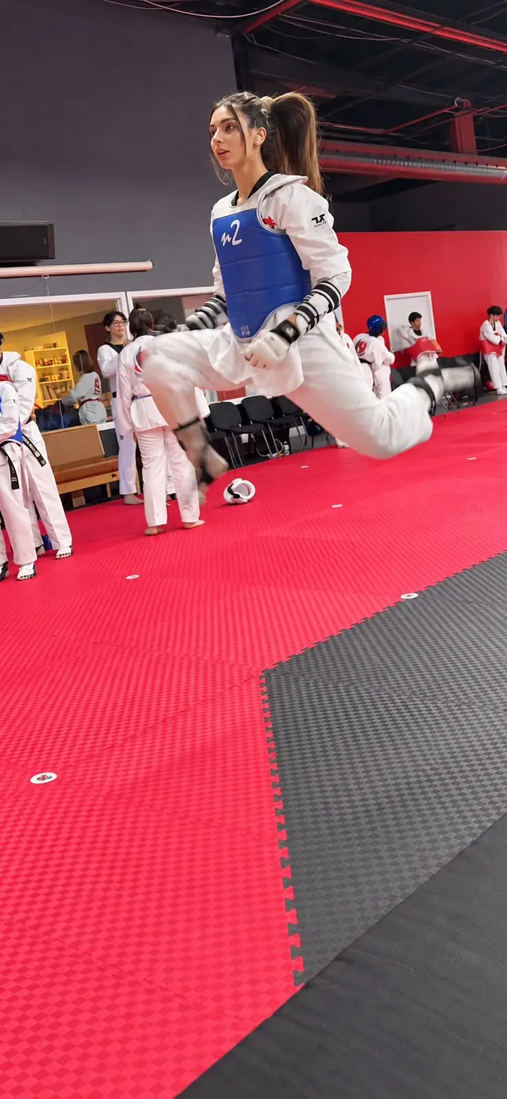A Dragon Taekwondo athlete in a blue chest protector in the air mid-kick