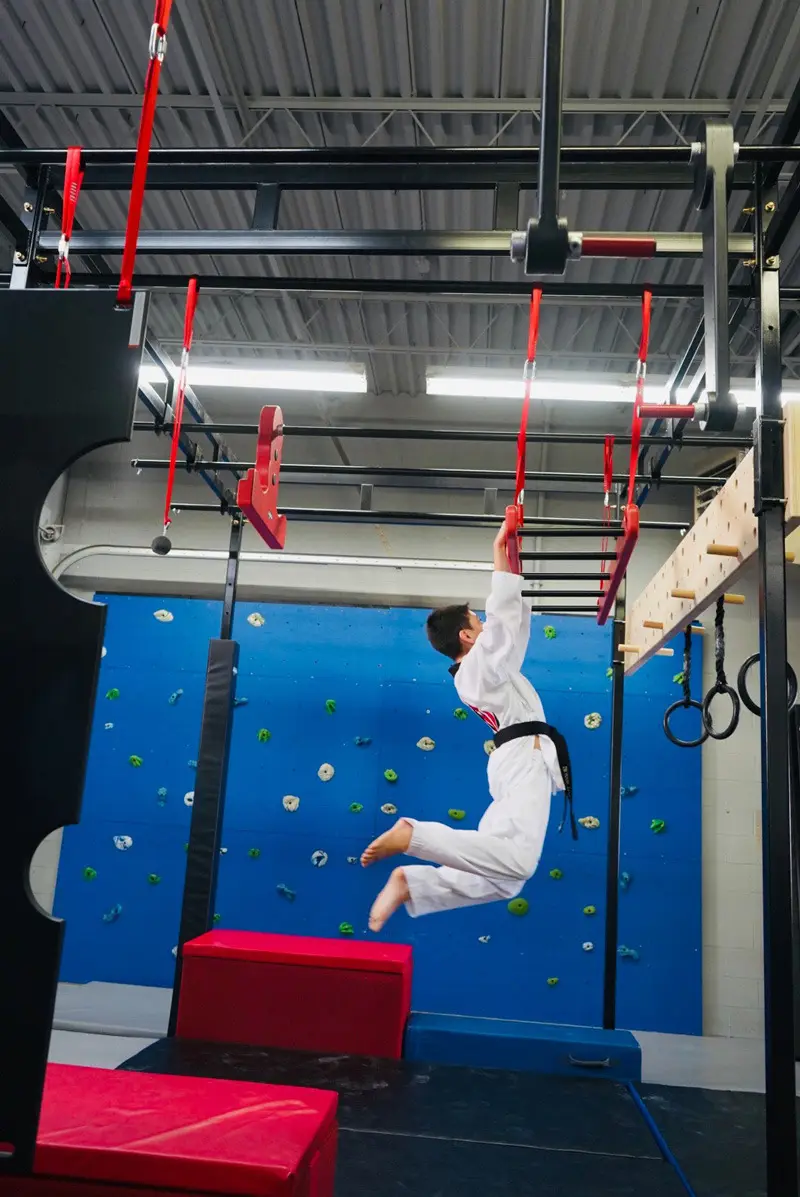 A student in a Dragon Taekwondo uniform crossing the rings on the indoor ninja course