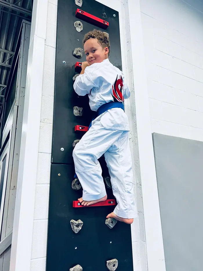 A young Dragon Taekwondo student climbing the peg wall on the ninja course
