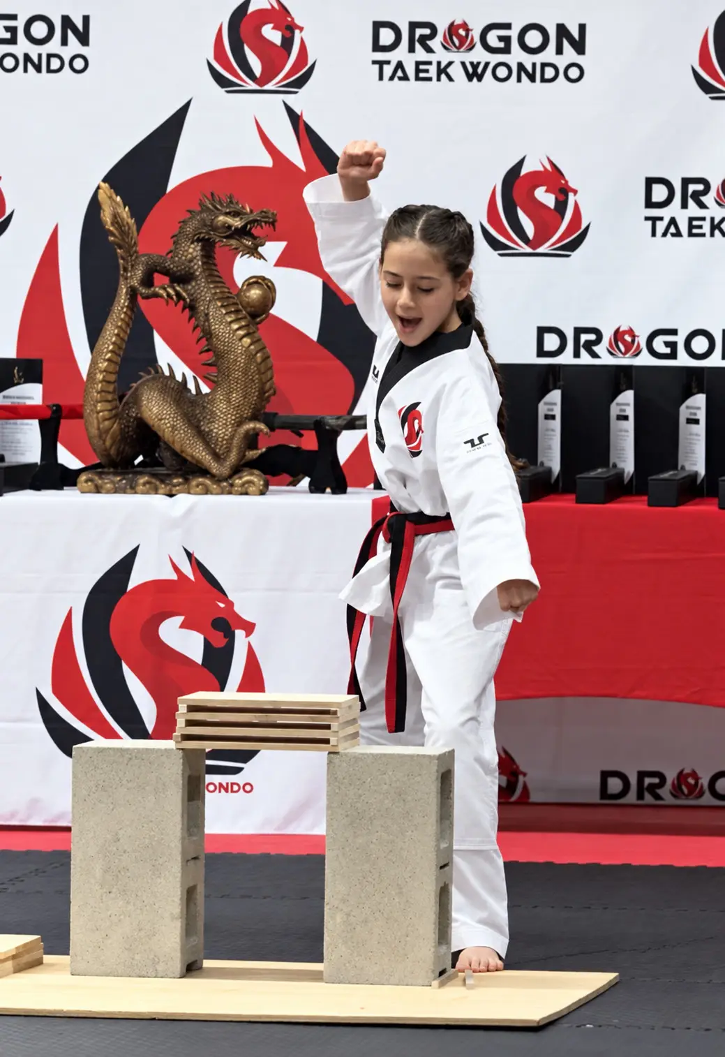 A student breaks a board in front of the Dragon Taekwondo backdrop