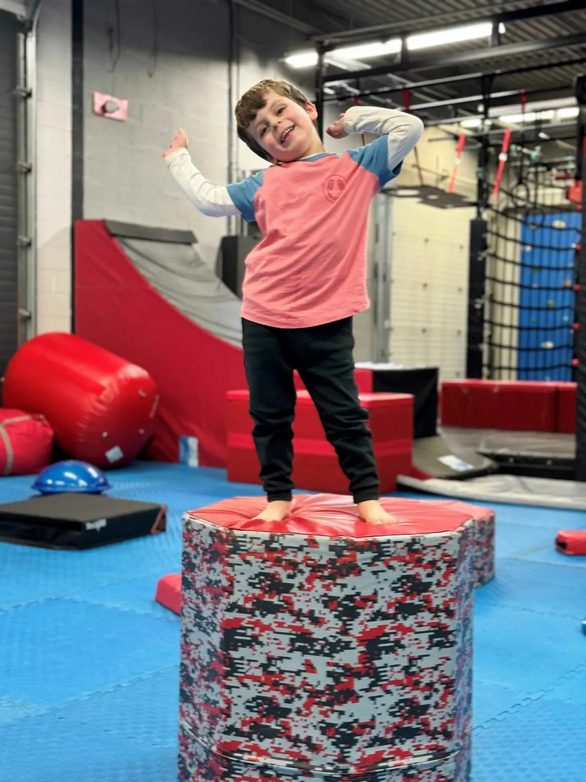 A smiling child striking a pose on a soft pad on the indoor ninja course