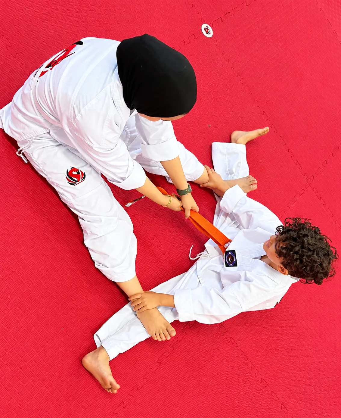 A young student stretching on the mats with a partner’s help