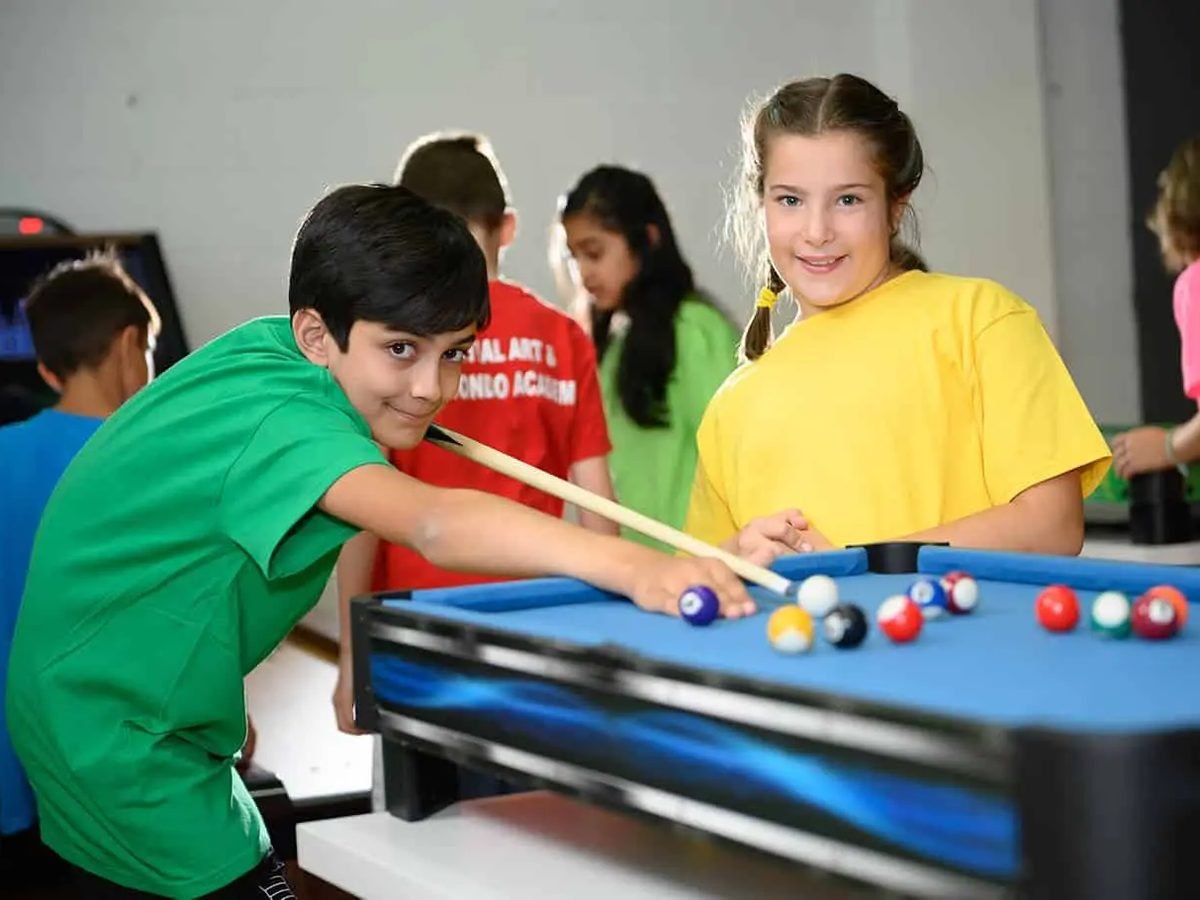 Smiling kids in bright T-shirts playing pool