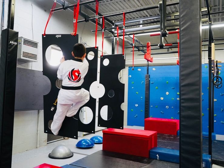 A student climbing through the holey wall on the ninja course